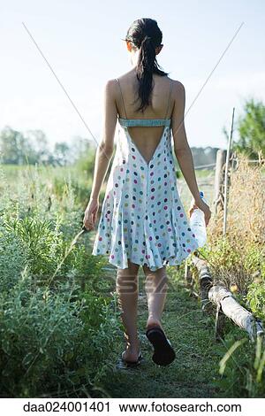 Stock Image - Young woman walking through garden with bottle of water, rear view. Fotosearch