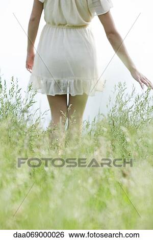 Stock Photograph - Young woman walking through tall grass, cropped. Fotosearch