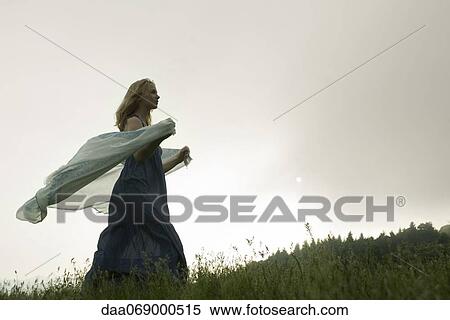 Young woman walking through tall grass, scarf blowing behind her in breeze View Large Photo Image Stock Photography - Young woman walking through tall grass, scarf blowing behind her in breeze. Fotosearch