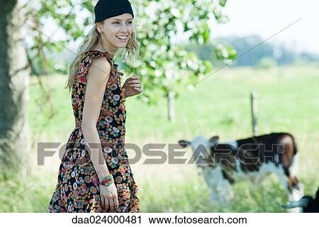 Stock Image - Young woman walking toward cow, smiling, looking away. Fotosearch