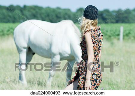 Stock Image - Young woman walking toward horse, rear view. Fotosearch