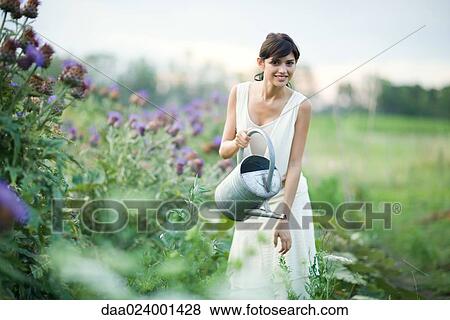 Young woman watering plants in garden with watering can, smiling at camera View Large Photo Image Stock Photo - Young woman watering plants in garden with watering can, smiling at camera. Fotosearch