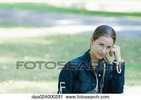 Young woman wearing jacket, leaning head on hand, smiling at camera View Large Photo Image Stock Image - Young woman wearing jacket, leaning head on hand, smiling at camera. Fotosearch
