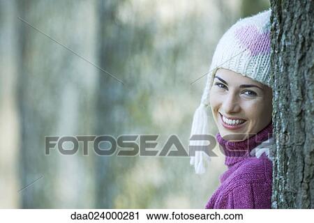 Young woman wearing knit hat, leaning against tree, smiling over shoulder at camera View Large Photo Image Stock Image - Young woman wearing knit hat, leaning against tree, smiling over shoulder at camera. Fotosearch