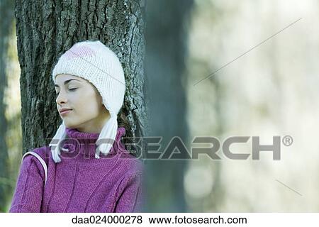 Young woman wearing knit hat, leaning against tree, eyes closed View Large Photo Image Stock Photo - Young woman wearing knit hat, leaning against tree, eyes closed. Fotosearch