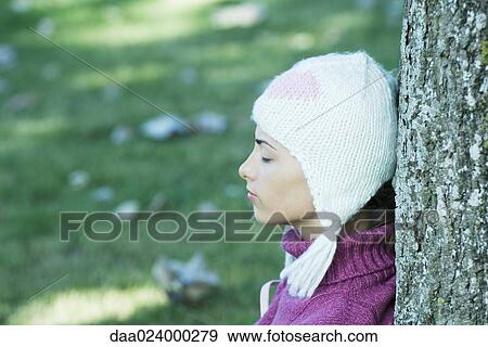 Young woman wearing knit hat, leaning against tree, eyes closed, side view View Large Photo Image Stock Photo - Young woman wearing knit hat, leaning against tree, eyes closed, side view. Fotosearch