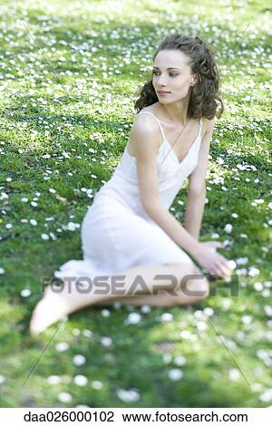 Stock Image - Young woman wearing slip, sitting in field of flowers, looking over shoulder, smiling. Fotosearch