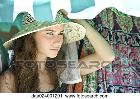 Stock Image - Young woman wearing straw hat, looking away. Fotosearch
