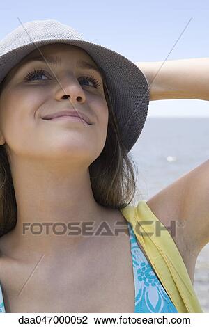 Young woman wearing sun hat, looking up and smiling, sea in background View Large Photo Image Stock Image - Young woman wearing sun hat, looking up and smiling, sea in background. Fotosearch