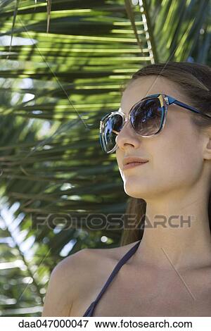 Young woman wearing sunglasses, palm leaves in background, portrait View Large Photo Image Stock Photo - Young woman wearing sunglasses, palm leaves in background, portrait. Fotosearch
