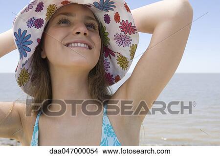 Young woman wearing sunhat at beach, looking up and smiling View Large Photo Image Picture - Young woman wearing sunhat at beach, looking up and smiling. Fotosearch