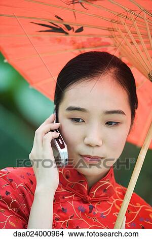 Young woman wearing traditional Chinese clothing, holding parasol and using cell phone View Large Photo Image Picture - Young woman wearing traditional Chinese clothing, holding parasol and using cell phone. Fotosearch
