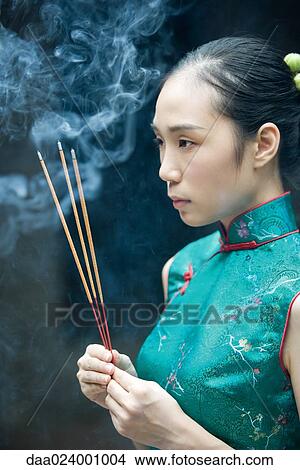 Young woman wearing traditional Chinese clothing, holding up incense, side view View Large Photo Image Picture - Young woman wearing traditional Chinese clothing, holding up incense, side view. Fotosearch