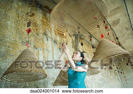 Young woman wearing traditional Chinese clothing, lighting spiral of incense, low angle view View Large Photo Image Picture - Young woman wearing traditional Chinese clothing, lighting spiral of incense, low angle view. Fotosearch