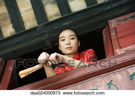Young woman wearing traditional Chinese clothing, holding fan, leaning on windowsill, low angle view View Large Photo Image Stock Image - Young woman wearing traditional Chinese clothing, holding fan, leaning on windowsill, low angle view. Fotosearch