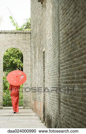 Stock Image - Young woman wearing traditional Chinese clothing, walking with parasol, rear view. Fotosearch