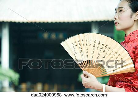 Young woman wearing traditional Chinese clothing, holding fan, looking up View Large Photo Image Stock Photo - Young woman wearing traditional Chinese clothing, holding fan, looking up. Fotosearch