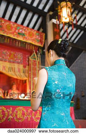 Stock Photo - Young woman wearing traditional Chinese clothing, holding incense in temple. Fotosearch