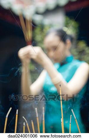 Young woman wearing traditional Chinese clothing, holding up incense, focus on incense in foreground View Large Photo Image Stock Photograph - Young woman wearing traditional Chinese clothing, holding up incense, focus on incense in foreground. Fotosearch