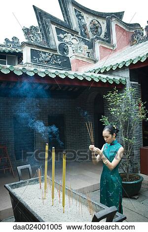 Stock Photography - Young woman wearing traditional Chinese clothing, holding up incense in temple courtyard. Fotosearch