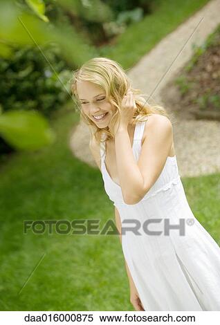 Stock Photography - Young woman wearing white dress, hand in hair. Fotosearch