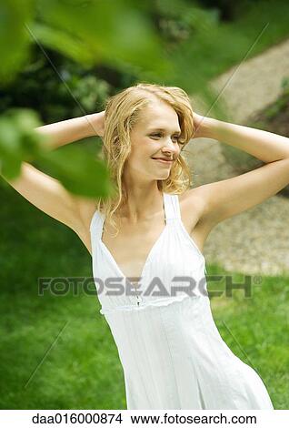 Young woman wearing white dress, hands behind head View Large Photo Image Picture - Young woman wearing white dress, hands behind head. Fotosearch