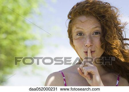 Stock Image - Young woman with finger on lips, portrait. Fotosearch