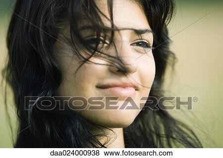 Stock Photo - Young woman with hair blowing across her face, smiling, portrait. Fotosearch