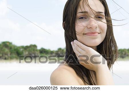 Stock Photography - Young woman with hair tousled by wind, smiling at camera, close-up. Fotosearch