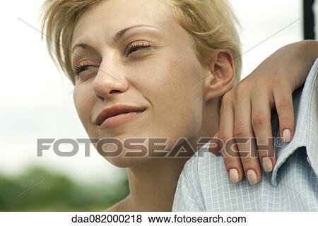 Stock Photo - Young woman with hand on man's shoulder, looking away and smiling. Fotosearch