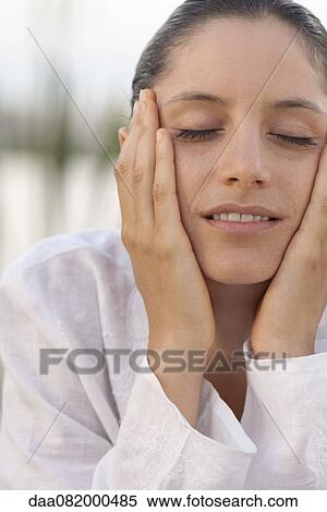 Stock Photography - Young woman with hands on face and eyes closed, portrait. Fotosearch