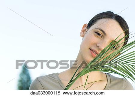 Young woman with palm leaf, smiling at camera View Large Photo Image Stock Photography - Young woman with palm leaf, smiling at camera. Fotosearch