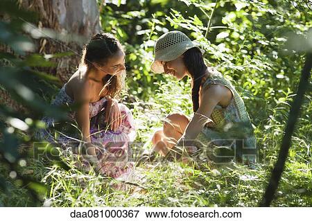 Stock Photo - Young women crouching in woods, face to face. Fotosearch