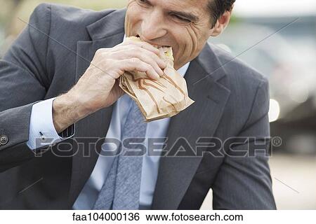 Businessman eating sandwich on the move View Large Photo Image Stock Photograph - Businessman eating sandwich on the move. Fotosearch