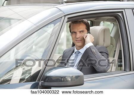 Stock Image - Businessman using cell phone while driving car. Fotosearch
