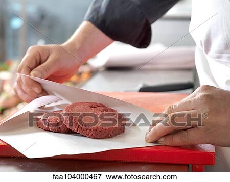 Stock Photo - Butcher wrapping beef patties in wax paper, cropped. Fotosearch