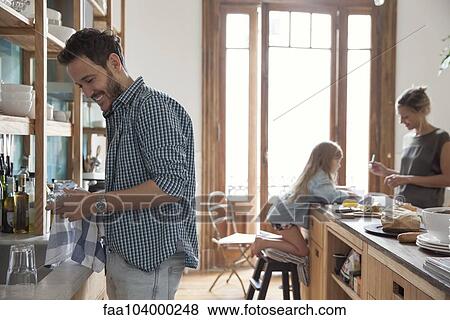 Stock Photo - Family in kitchen, man drying dishes in foreground. Fotosearch