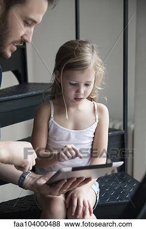 Stock Photo - Father showing young daughter how to use digital tablet. Fotosearch