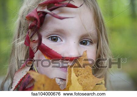 Stock Photograph - Girl holding autumn leaves in front of her face, portrait. Fotosearch