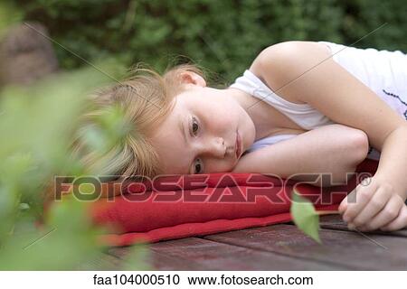 Stock Image - Girl lying on cushion outdoors with leaf in hand. Fotosearch