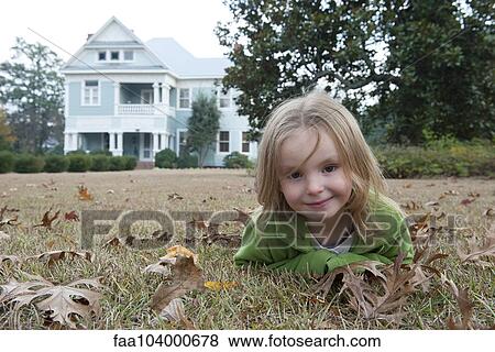 Stock Photo - Girl lying on stomach on lawn, smiling, portrait. Fotosearch