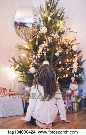 Picture - Girl sitting on floor gazing up at Christmas tree. Fotosearch