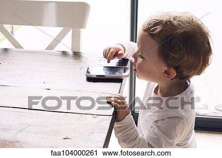 Little boy playing with smartphone left on edge of table View Large Photo Image Stock Image - Little boy playing with smartphone left on edge of table. Fotosearch
