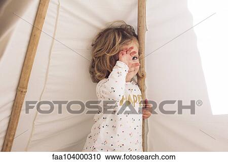 Stock Image - Little girl covering face with hand, smiling shyly. Fotosearch