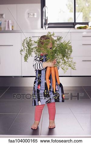 Stock Photography - Little girl holding large carrots in front of face. Fotosearch