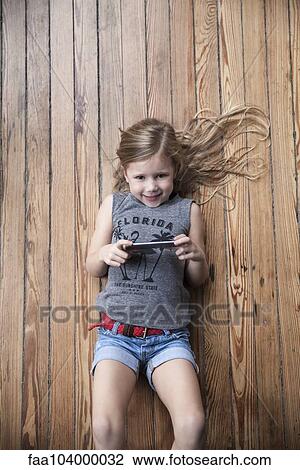 Stock Image - Little girl lying on floor using smartphone. Fotosearch