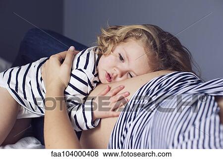 Stock Photo - Little girl resting her head and hand on mother's pregnant stomach. Fotosearch