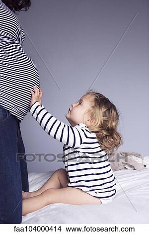 Picture - Little girl touching mother's pregnant stomach, cropped. Fotosearch