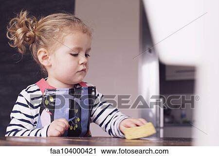 Stock Image - Little girl wiping table with spong. Fotosearch