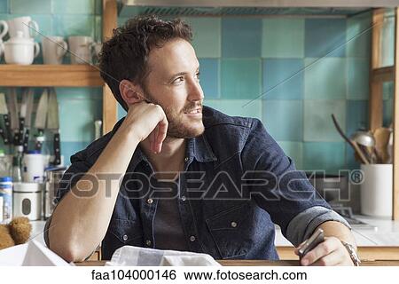 Stock Photograph - Man daydreaming in messy kitchen. Fotosearch